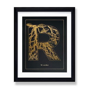 May include: A black and gold framed print with a gold foil illustration of the letter "R" formed by a stylized root system. The text "'R' is for Root" is printed below the illustration.