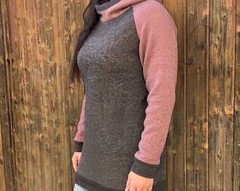 Puede incluir: Una sudadera con capucha de manga larga que presenta un torso gris carbón jaspeado y mangas de color rosa malva. La prenda incluye una capucha alta y gruesa estilo cuello alto, puños acanalados gris oscuro y un dobladillo a juego.