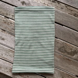 May include: A green and white striped neck gaiter, a tube-shaped accessory. The fabric has horizontal stripes of light green and white. The gaiter is laying on a weathered wooden surface.