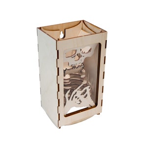 May include: A wooden box with a skeleton design cut out of the front. The box is made of light wood and has a clear plastic window in the front.