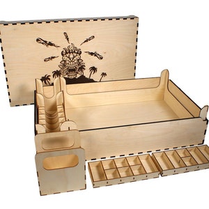 May include: Wooden box with a laser-cut design of a tiki head with flames and palm trees on the lid. The box has dividers and trays for organizing game pieces.