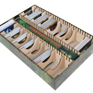 May include: A wooden game organizer with multiple compartments for storing cards and a long, narrow compartment for storing a game board or other components. The organizer is made of light brown wood and has a green and brown patterned design.
