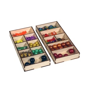 May include: Two wooden organizer trays with compartments for storing game pieces. The top tray has a variety of colored plastic game pieces, dice, and tokens. The bottom tray has black and green game pieces.