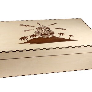 May include: A wooden box with a brown tiki head design on the lid. The box has a black and white checkered border around the edge.