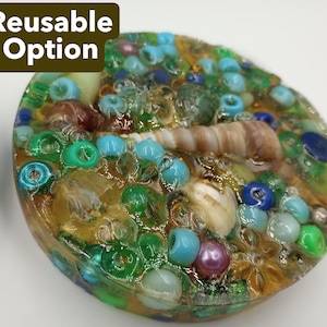 Puede incluir: Un objeto decorativo redondo con una mezcla de cuentas coloridas, pequeñas conchas marinas y otros adornos. El objeto está incrustado en resina transparente, con el texto "Reusable Option" en un cuadro verde oscuro en la esquina superior izquierda.