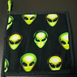 May include: Black fabric dishcloth with a green alien pattern. The aliens have large eyes and are green with a glow effect.