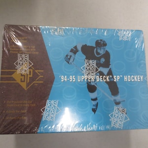 Puede incluir: Una caja de cartas de hockey Upper Deck SP de 1994-95 con un jugador de hockey con un uniforme azul y blanco en la parte delantera. La caja es azul y blanca con el logotipo de Upper Deck y el texto "'94-95 Upper Deck SP Hockey".