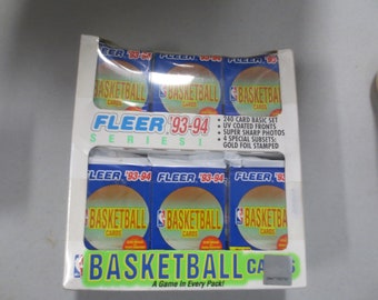 Può includere: Una scatola di carte da basket Fleer '93-94 Serie 1. La scatola contiene più pacchetti con il logo NBA e le parole "Basketball Cards". La scatola ha anche il testo "240 Card Basic Set" e "Gold Foil Stamped".