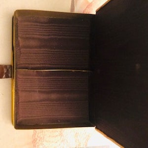 May include: An empty, brown, rectangular box with a hinged lid and a leather strap. The box is lined with brown fabric.
