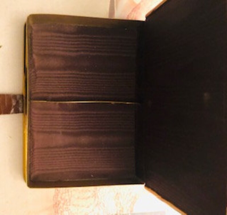 May include: An empty, brown, rectangular box with a hinged lid and a leather strap. The box is lined with brown fabric.