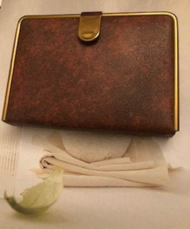 May include: A brown leather jewelry box with a gold trim and a gold clasp. The box is closed.