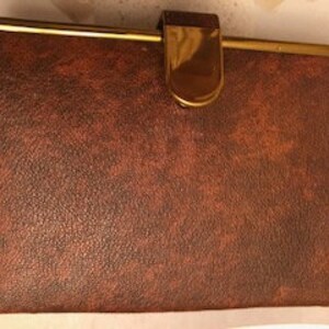 May include: A brown leatherette case with a gold trim and a gold clasp. The case has a textured surface.