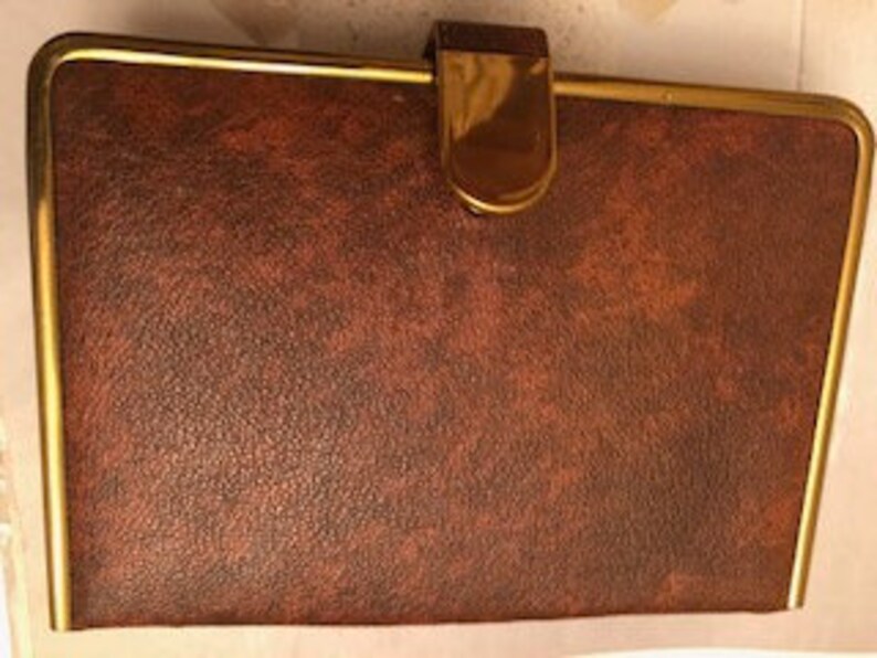 May include: A brown leatherette case with a gold trim and a gold clasp. The case has a textured surface.