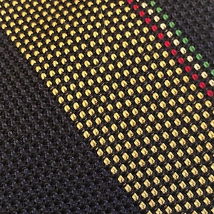 May include: Close-up of a textured fabric with a diagonal stripe pattern. The pattern features a navy blue background with a yellow and black dotted stripe, and a thin stripe of red and green dots.