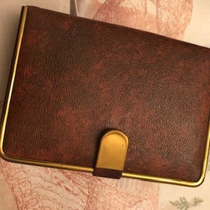 May include: A brown leatherette wallet with a gold trim and a gold metal clasp.