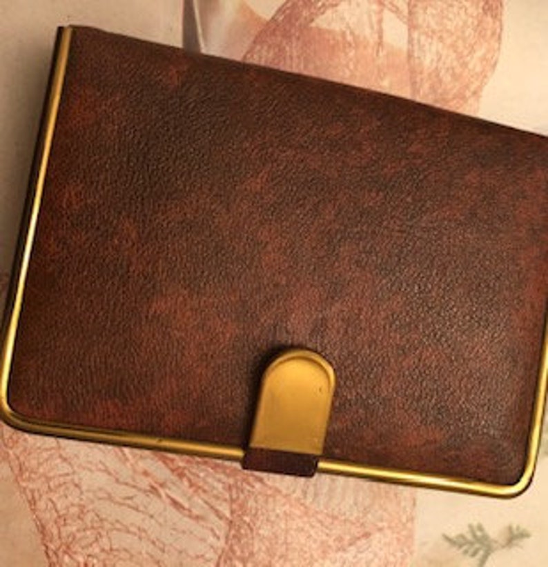 May include: A brown leatherette wallet with a gold trim and a gold metal clasp.