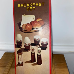 May include: A red box with the words "Breakfast Set" in yellow letters. The box shows a set of miniature breakfast items, including a wooden hourglass, salt and pepper shakers, and egg cups with floral designs.