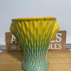 May include: A yellow and green ceramic vase with a textured surface and two handles. The vase is on a wooden surface.