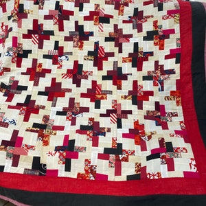 May include: A patchwork quilt with a white background and red, black, and pink squares. The quilt is made of different fabrics and has a red border.