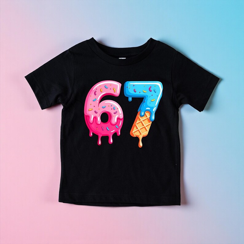 May include: Black t-shirt featuring a colorful graphic of the number 67. The number 6 is designed like a pink donut with sprinkles, and the number 7 is designed like a blue ice cream cone with a waffle cone base. The shirt is likely for a child.