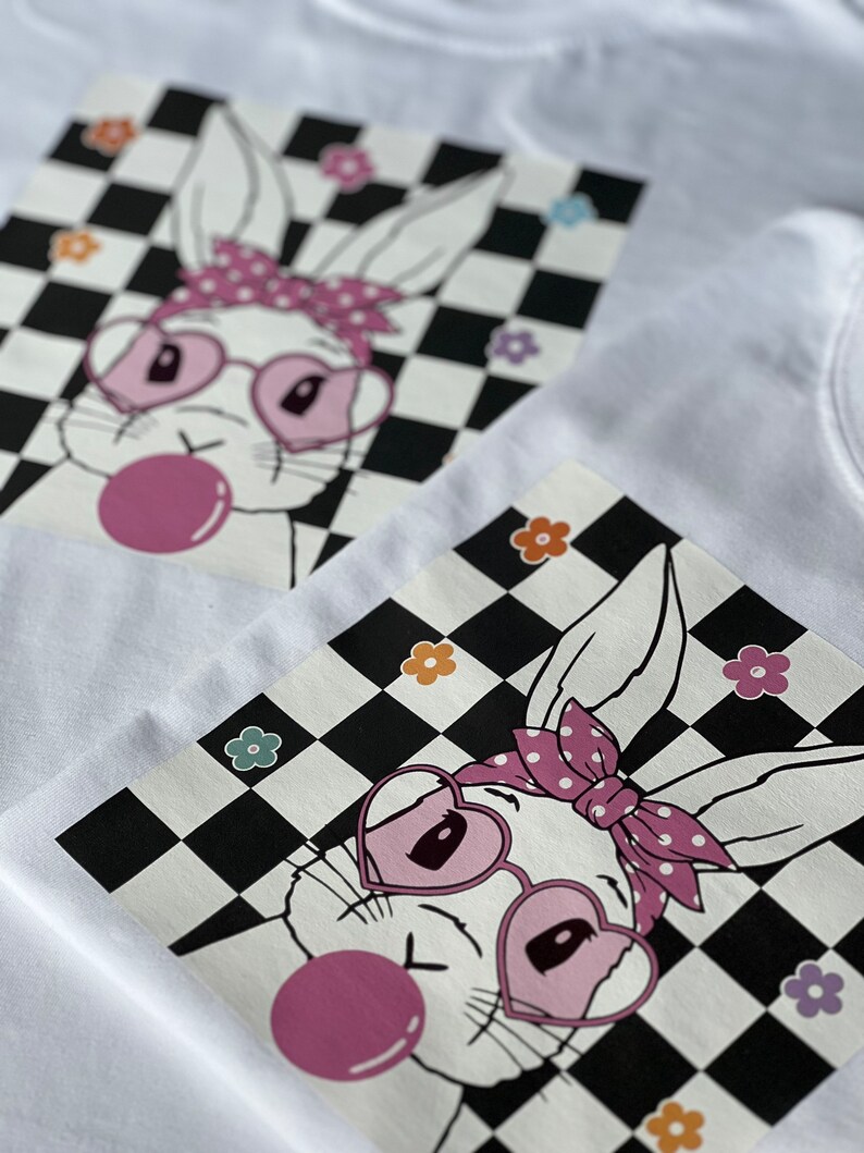 May include: A white bunny with pink heart-shaped sunglasses and a pink polka dot headband is blowing a pink bubble. The bunny is on a black and white chequered background with colourful flowers.