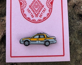 Pode incluir: Um cartão rosa com um desenho de mão de hamsa vermelho e as palavras "Classic Tattoo" em um círculo ao redor da mão. Um alfinete de carro amarelo e cinza está abaixo do hamsa.
