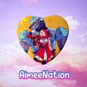 May include: A heart-shaped pin with a cartoon illustration of a wolf wearing a blue and white patterned shirt and a red-hooded girl holding a gun. The background is a yellow heart with a glittery effect. The text "AimeeNation" is printed below the pin.