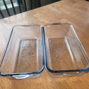 Peut inclure: Deux moules à pain en verre transparent avec des bords bleus. Les moules sont vides et posés sur une surface en bois.