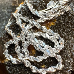 May include: A silver rope chain necklace with a clasp. The chain is made of small, twisted links.
