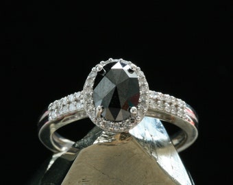 May include: A silver ring with a black oval-shaped gemstone surrounded by a halo of smaller white gemstones.
