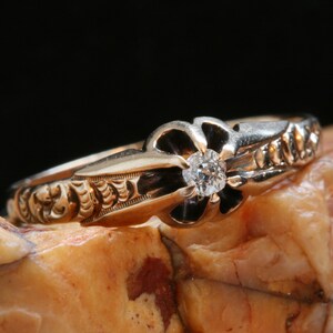 May include: A gold ring with a single diamond set in a flower-shaped design. The ring is detailed with intricate floral engravings.