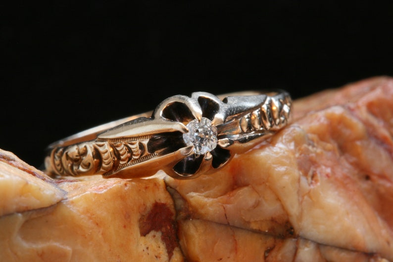May include: A gold ring with a single diamond set in a flower-shaped design. The ring is detailed with intricate floral engravings.
