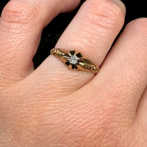 May include: A gold ring with a single diamond set in a flower-shaped design. The band is decorated with a textured pattern.