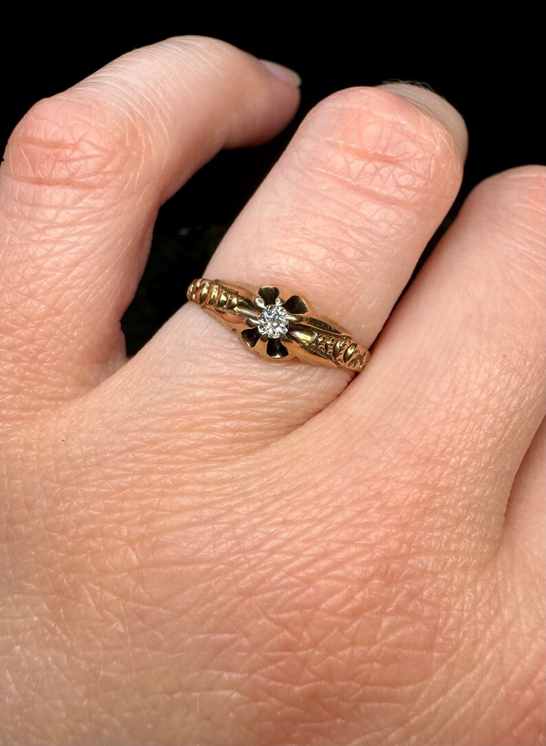 May include: A gold ring with a single diamond set in a flower-shaped design. The band is decorated with a textured pattern.