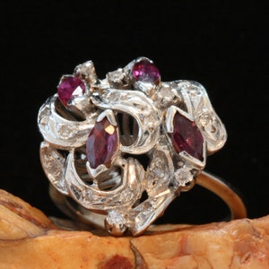 May include: A silver ring with a delicate, intricate design featuring multiple marquise-shaped ruby gemstones and smaller diamonds. The ring has a floral motif and a polished finish.