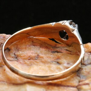 May include: A gold ring with a single diamond set in a delicate, ornate setting. The ring is shown from the underside, revealing the smooth, polished band.
