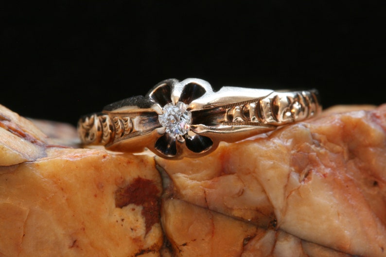 May include: A gold ring with a single diamond set in a flower-shaped design. The band is decorated with intricate floral engravings.
