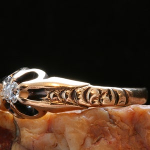 May include: A gold ring with a single diamond set in a claw setting. The ring has an intricate design with floral motifs.