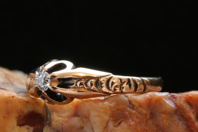 May include: A gold ring with a single diamond set in a claw setting. The ring has an intricate design with floral motifs.