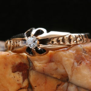 May include: A gold ring with a black enamel flower design and a single diamond in the center.