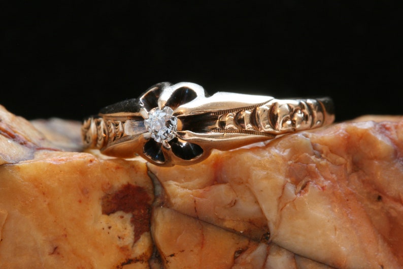 May include: A gold ring with a black enamel flower design and a single diamond in the center.