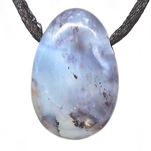 Op de afbeelding: Ovale hanger met een lichtblauw en grijs gemarmerd patroon. De steen hangt aan een donkerbruin koord. De hanger heeft een gepolijst, glad oppervlak tegen een witte achtergrond.