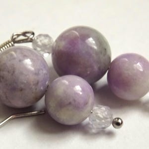 Puede incluir: Un par de pendientes con cuentas redondas de color lavanda y cuentas de cristal transparentes. Los pendientes están hechos de metal plateado.
