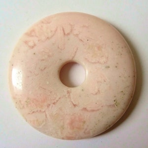 Puede incluir: Una piedra rosa en forma de donut con un agujero en el centro. La piedra tiene un patrón de mármol con remolinos blancos y rosados.