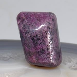 May include: A smooth, polished purple and black gemstone with a unique, irregular shape.