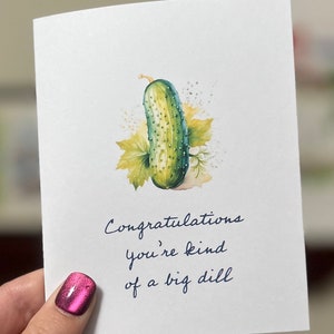 Peut inclure: Une carte blanche avec une illustration aquarelle verte d'un cornichon et le texte "Congratulations you're kind of a big dill".