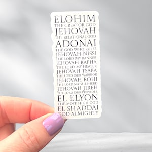 May include: A white sticker with black text listing various names of God, including Elohim, Jehovah, and Adonai. The sticker is held by a hand with a purple painted fingernail. The text describes the attributes of each name.