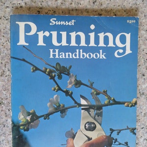 May include: A book titled "Sunset Pruning Handbook" with a blue cover and a photo of a hand holding pruning shears cutting a branch of a flowering tree.