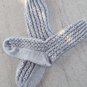 Può includere: Un paio di calzini di lana grigi con un motivo testurizzato. I calzini sono disposti su una superficie di cemento grigia.