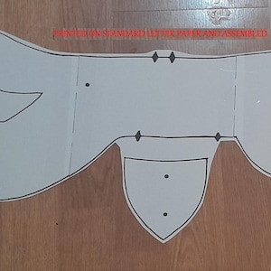 May include: A white paper craft pattern, printed on standard letter paper and assembled, with black outlines. The pattern includes shapes for a nose, tongue, and eyelashes. The text "PRINTED ON STANDARD LETTER PAPER AND ASSEMBLED" is visible.